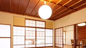 Ein traditioneller Raum mit Tatami-Matten, einem niedrigen Tisch, Kissen, großen Shoji-Bildschirmen und einer Deckenleuchte.
