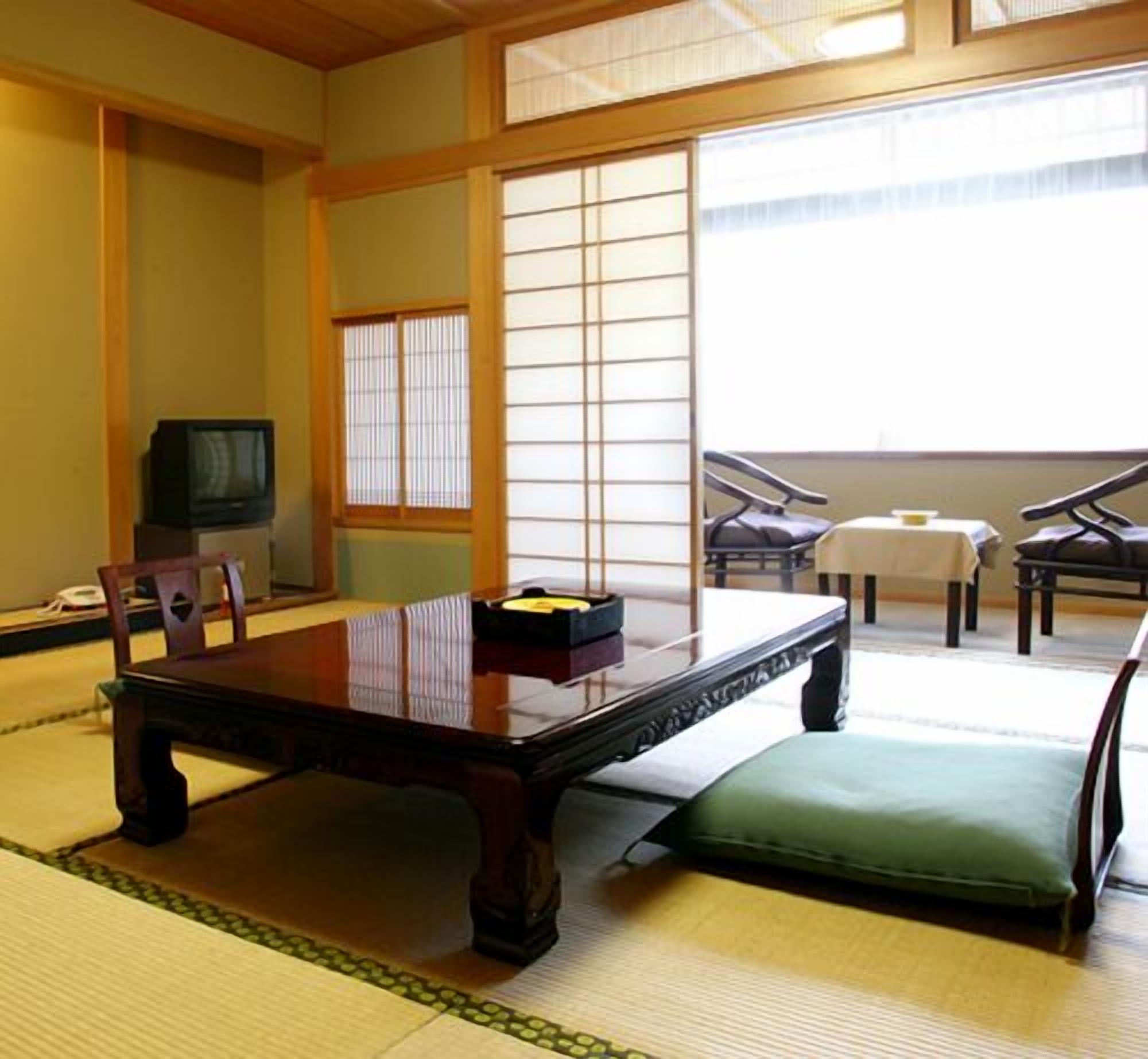 A traditional Japanese room with tatami flooring, a low table with a cushion, a television, and sliding doors.