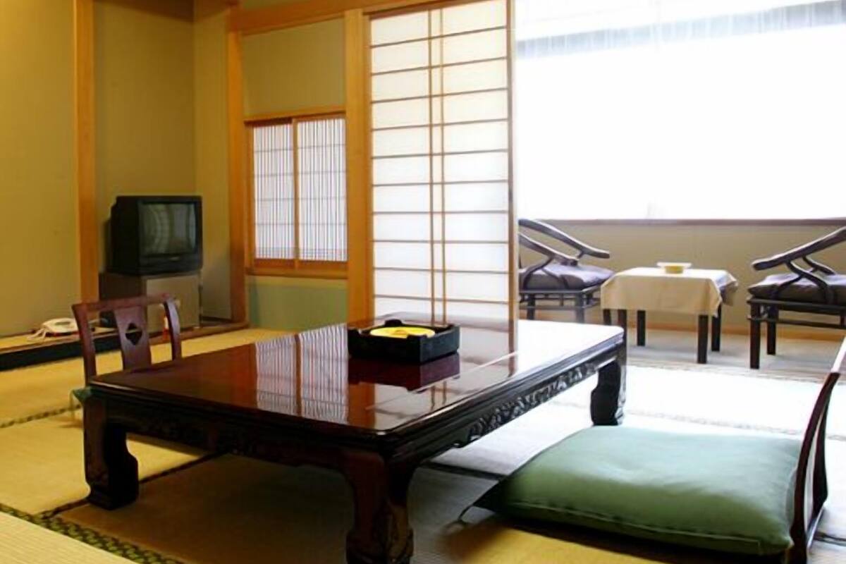 Une pièce de style japonais traditionnel, avec un sol recouvert de tatamis, une petite table basse avec un coussin, un téléviseur et des portes coulissantes.
