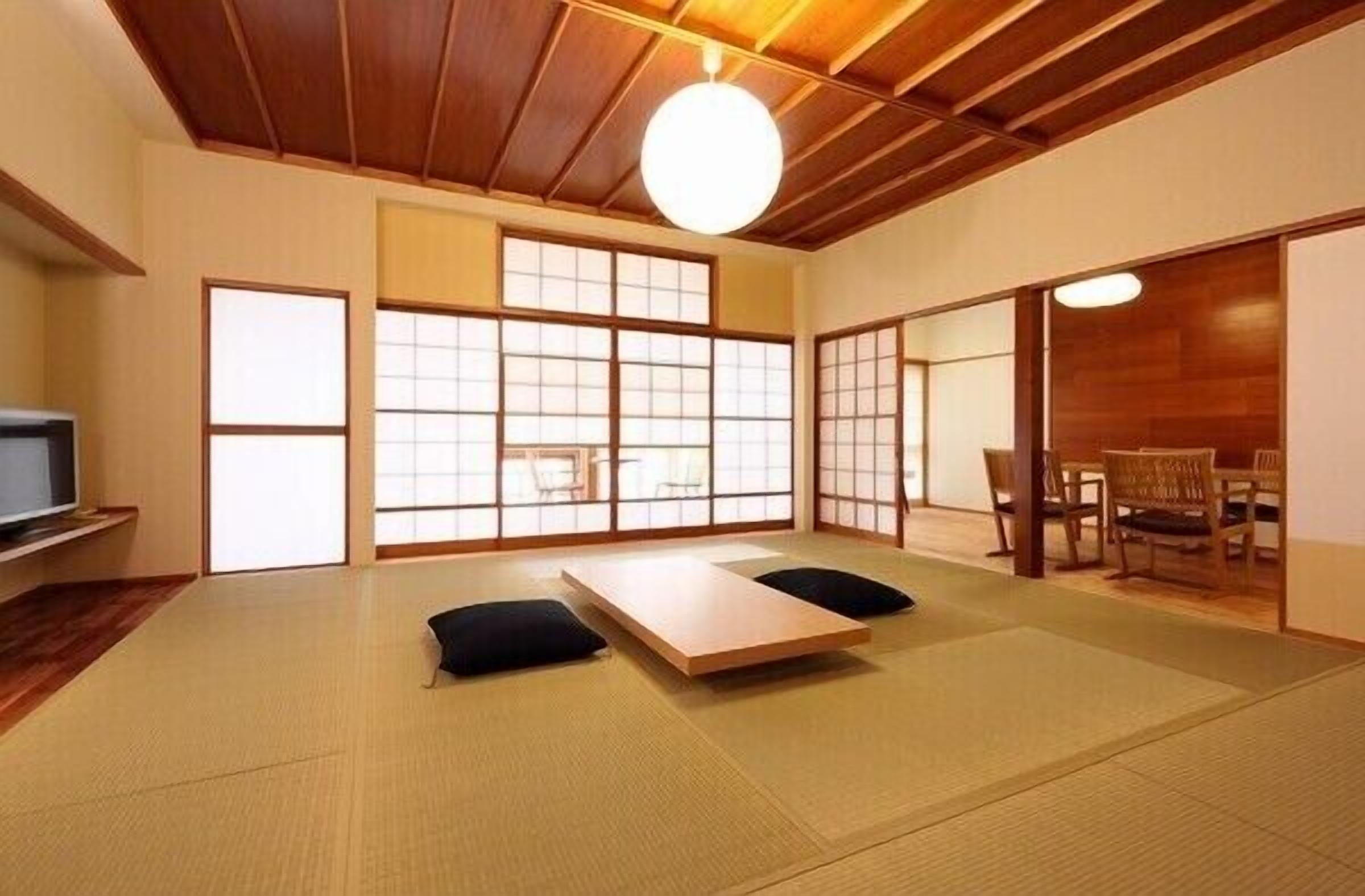 Een kamer met tatami matten, een lage tafel, kussens en een televisie.