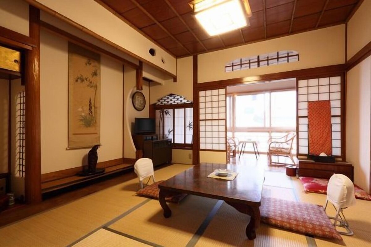A traditional Japanese room with tatami flooring, a low table, chairs, and sliding doors.