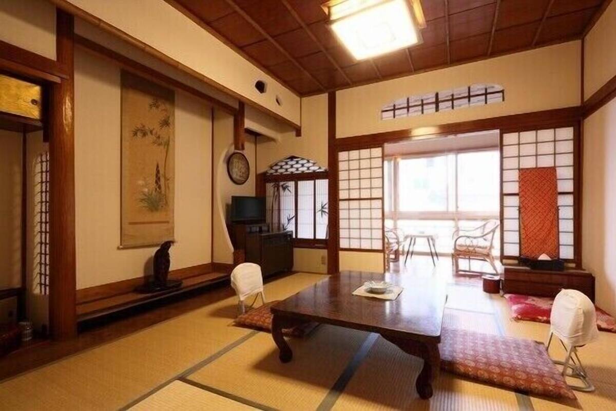 Une pièce de style japonais traditionnel, avec un sol recouvert de tatamis, une table basse, des chaises et des portes coulissantes.