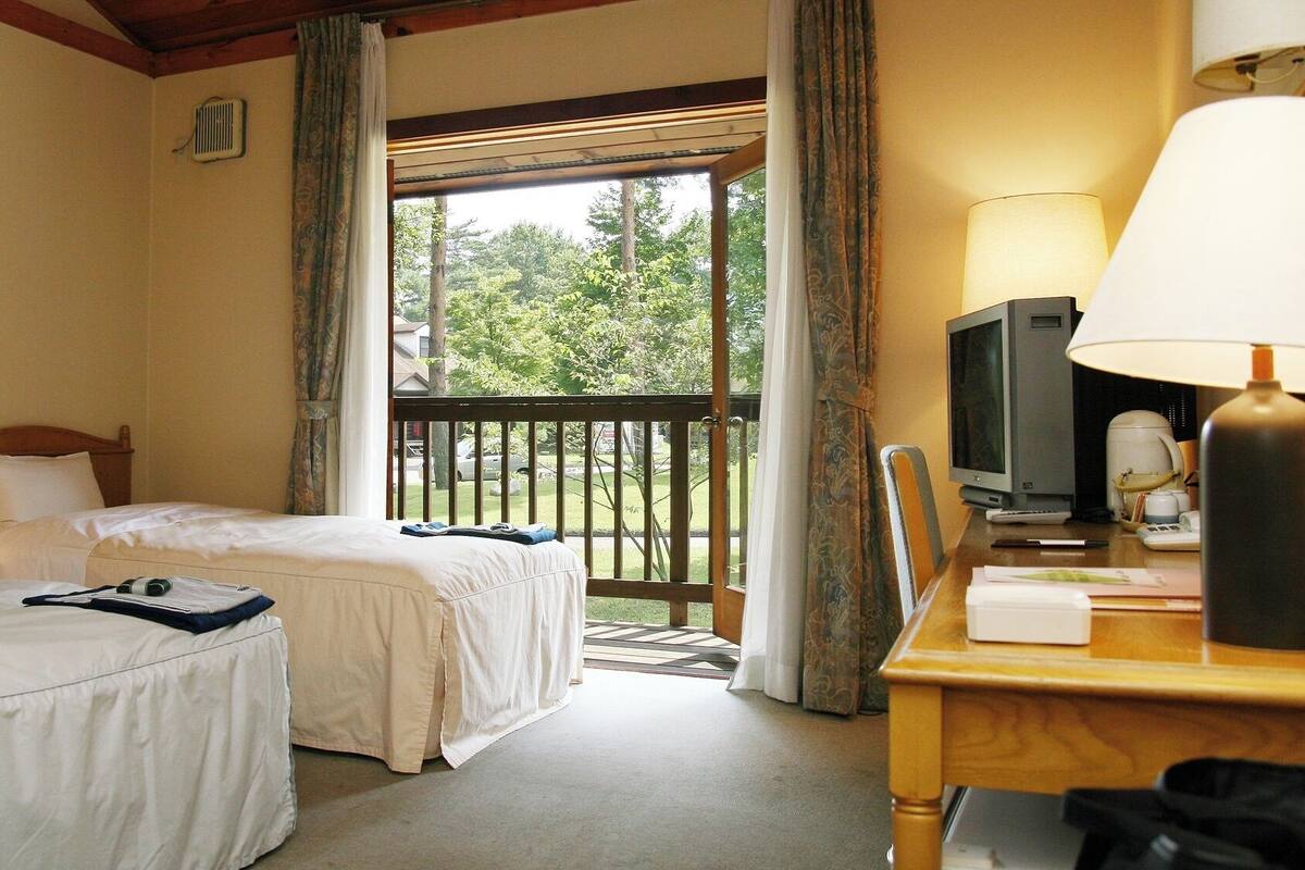 A hotel room with two beds, a desk with a lamp, a television, and a window with curtains.