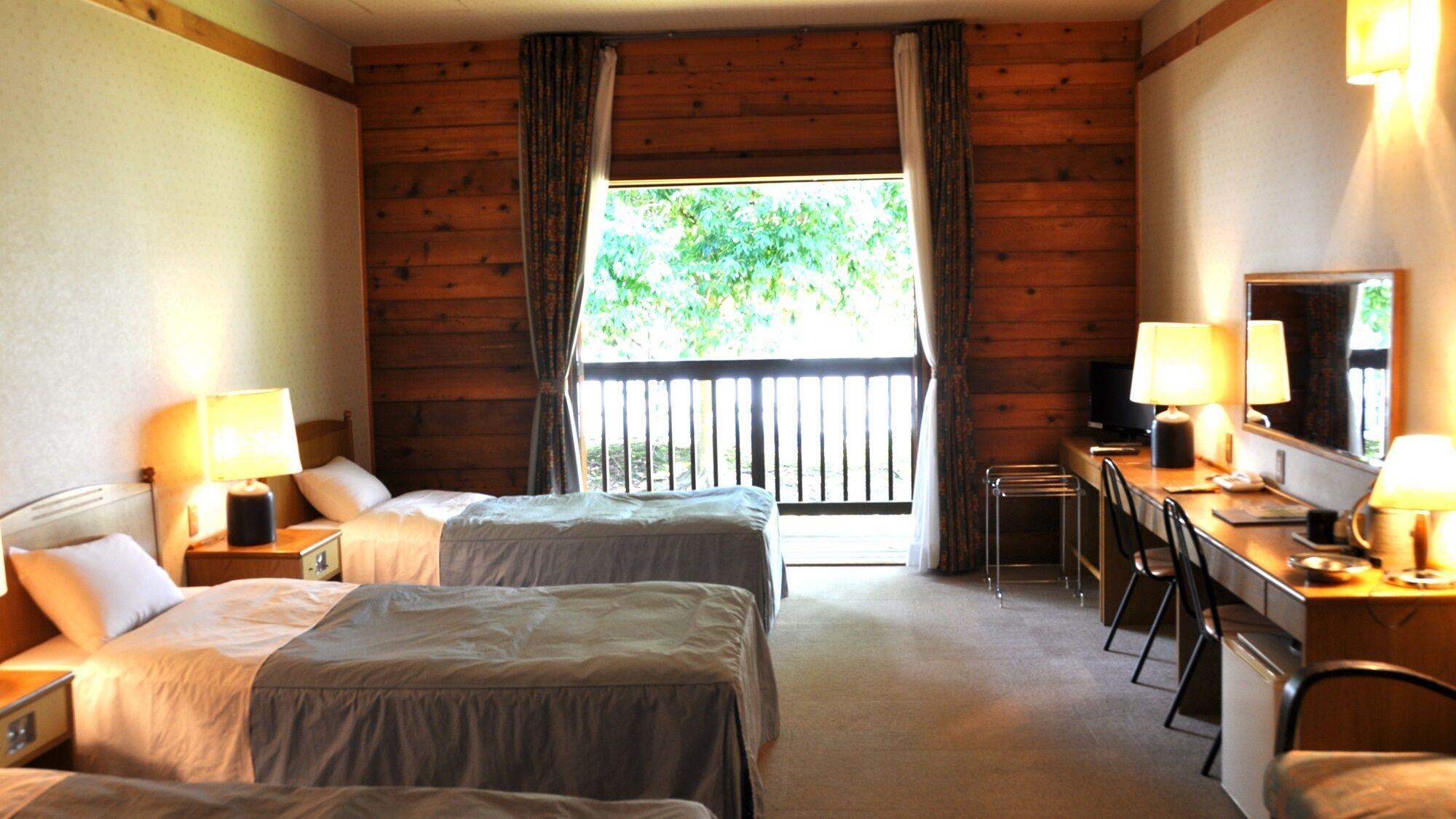 A room with two beds, a desk with a chair, a television, and a window with curtains.