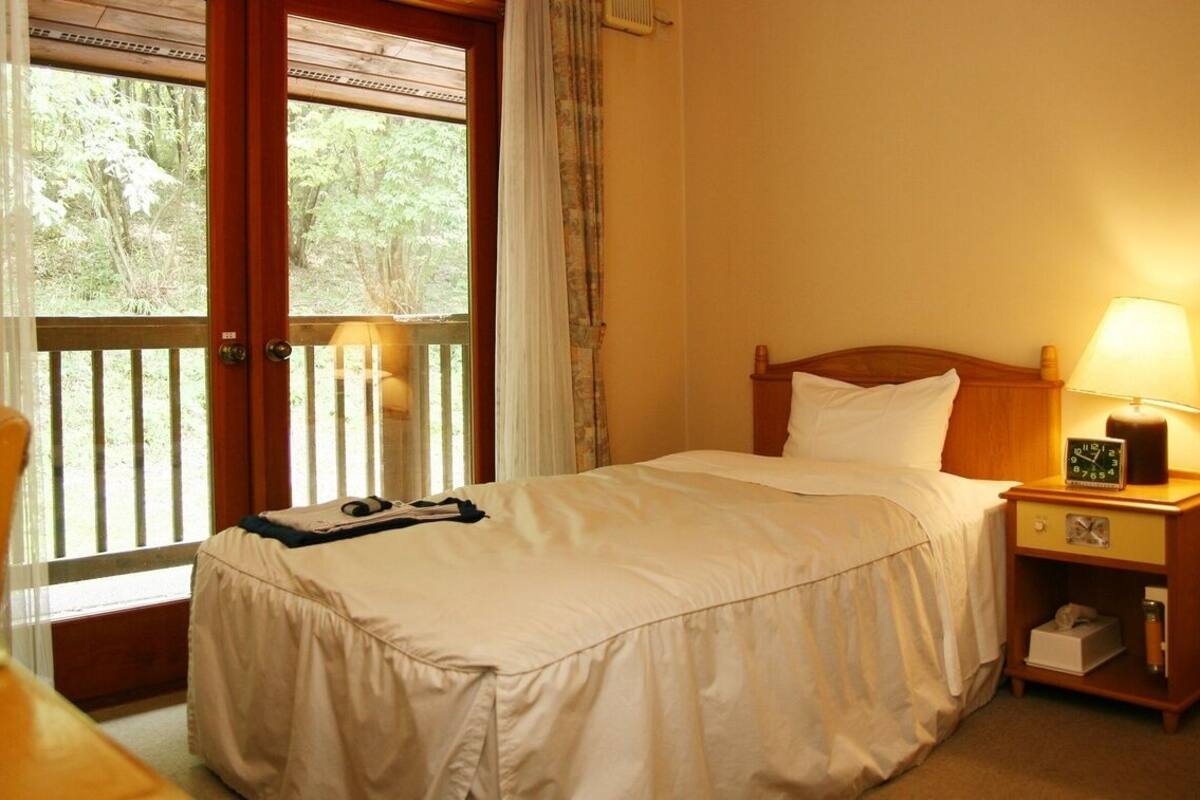 A hotel room with a bed, a nightstand with a lamp, a chair, and a window with curtains.