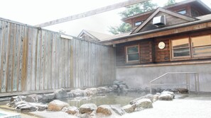 Eine Holzhütte mit Thermalquelle, einer Holzterrasse und einer Metalltreppe, die zu einem Fenster führt.