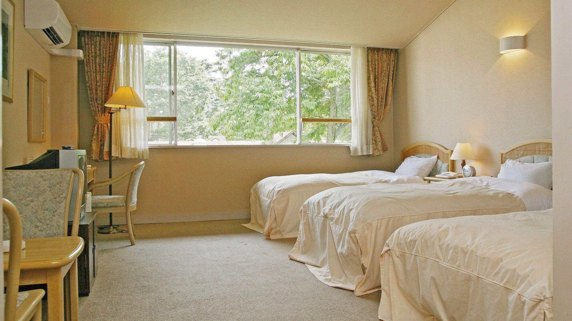 A hotel room with two beds, a desk, a chair, and a window with curtains.