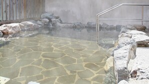 A hot spring area with stone tiles, rocks, and a metal railing.
