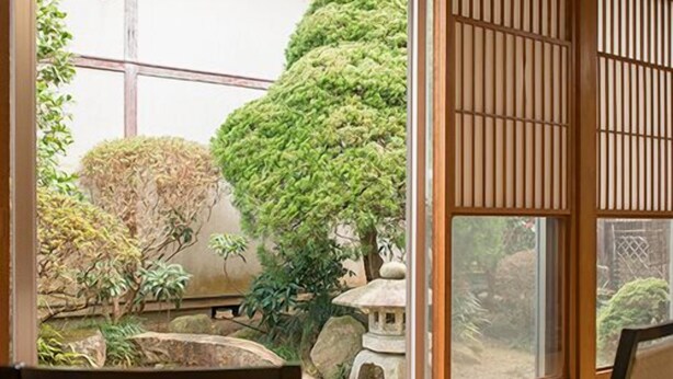 Une pièce de style japonais traditionnel, avec un sol recouvert de tatamis, un paravent coulissant de type shoji et une vue sur un jardin agrémenté d’un bassin et d’arbres.