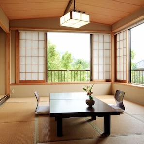 Une pièce avec un sol recouvert de tatamis, une petite table, une chaise et un luminaire suspendu.