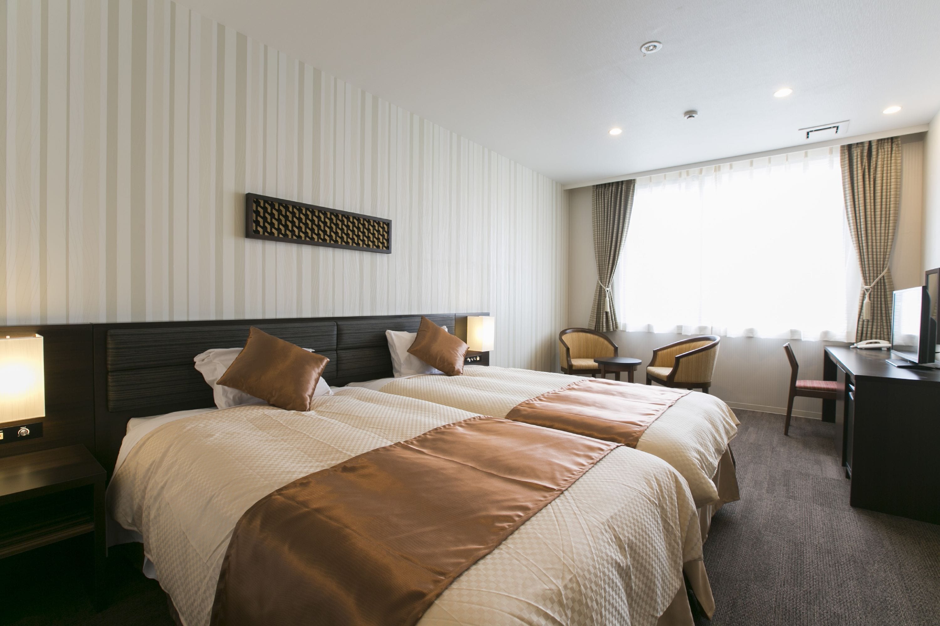 Une chambre d’hôtel avec deux lits, un bureau, une chaise et un téléviseur.