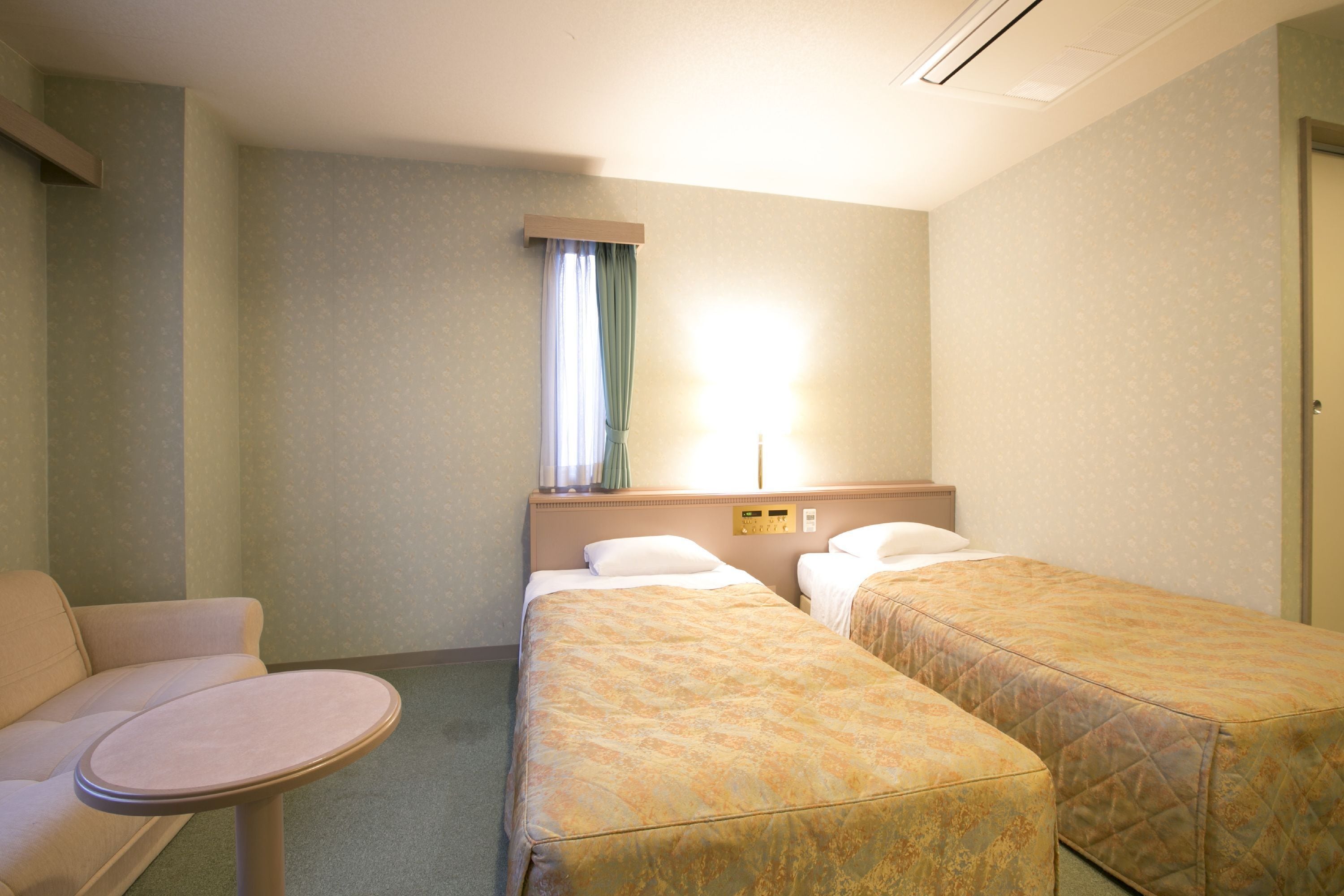 A hotel room with two single beds, a small round table, a sofa, and a window with curtains.