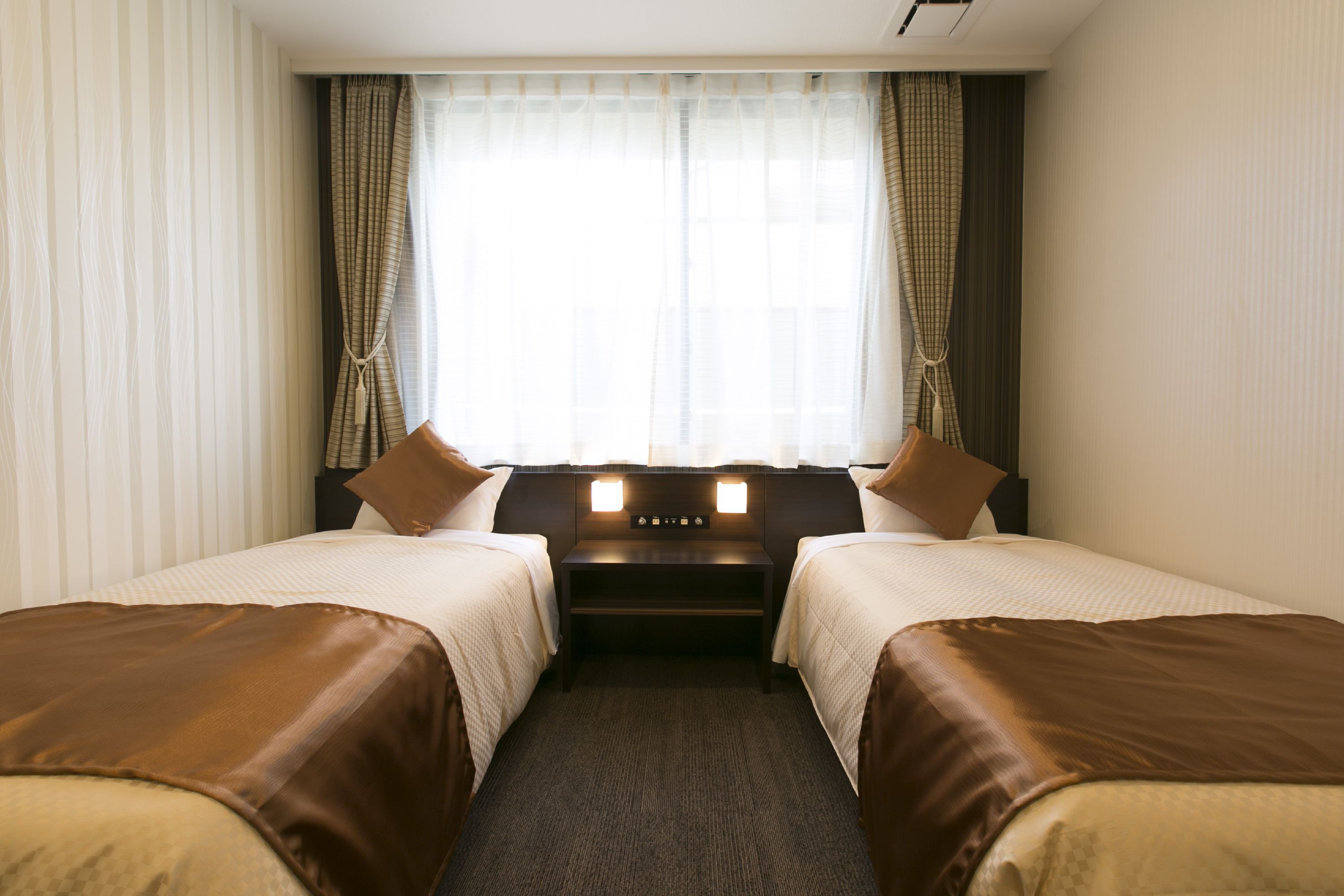A hotel room with two beds, a nightstand, and a window with curtains.