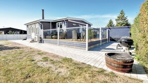 Une maison moderne dotée d’un patio entièrement vitré, d’un barbecue et d’un tonneau en bois.