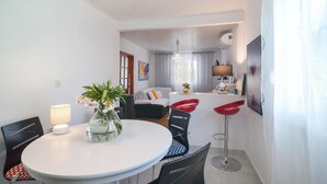 Een moderne woonkamer met een eettafel, stoelen, een bank en een keuken met een koelkast en een lamp.