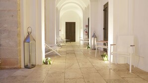 A corridor with white walls, a tiled floor, and a series of white chairs and tables. - I Pretti Resort (Favignana)