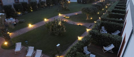 A courtyard with lounge chairs, a pathway, and a view of the sea.