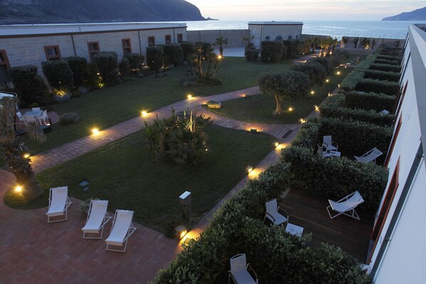 A courtyard with lounge chairs, a pathway, and a view of the sea. - I Pretti Resort (Favignana)