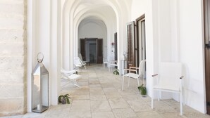 A corridor with white chairs and a lantern, leading to a door with shutters. - I Pretti Resort (Favignana)