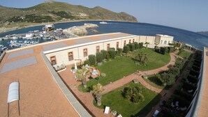 A coastal building with a patio area, a lawn, and a view of the sea and boats. - I Pretti Resort (Favignana)