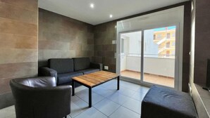 A modern living room with a sofa, a coffee table, and a balcony with a view of buildings.
