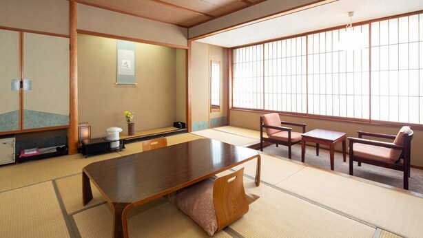 A traditional Japanese tatami room with a low table, two chairs, a small cabinet, and a sliding door. - Kirakuya Inn (Koriyama)