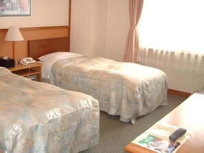 A hotel room with two beds, a desk with a lamp, a telephone, and a remote control on the desk. - Kirakuya Inn (Koriyama)