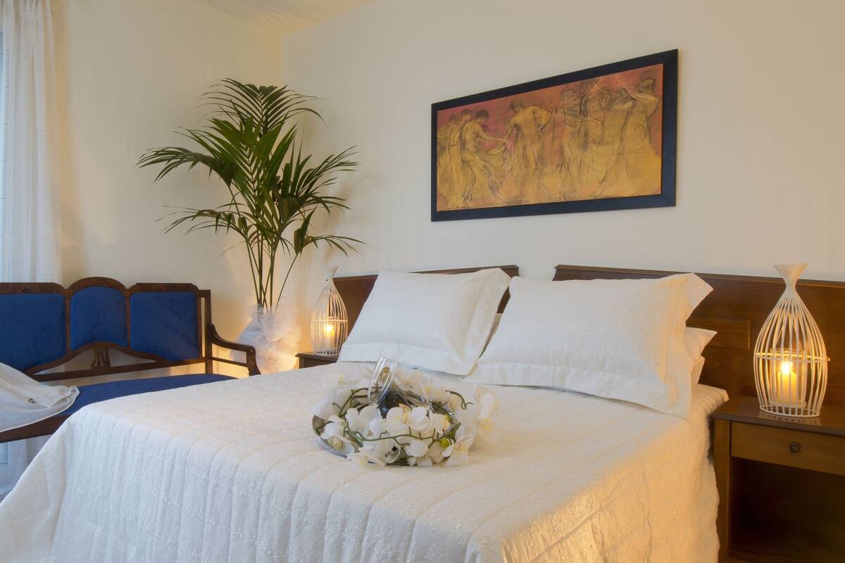 Habitación de hotel con cama, una silla, una mesita de noche, una lámpara y un cuadro en la pared.