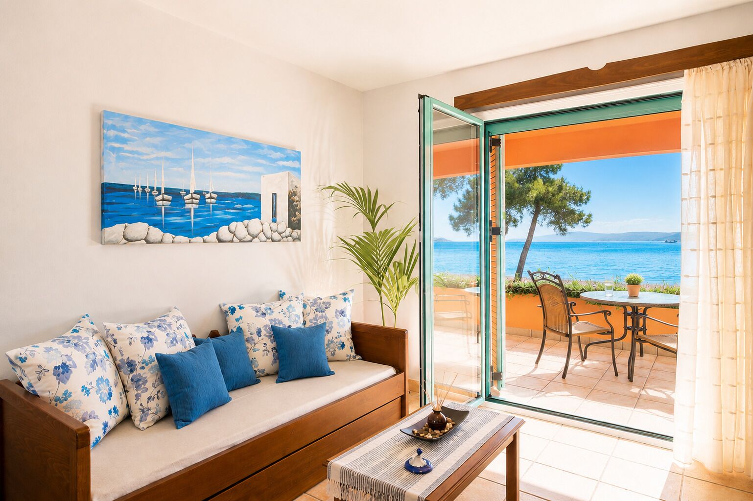 A living room with a sofa, a table, and a view of the sea through a glass door.