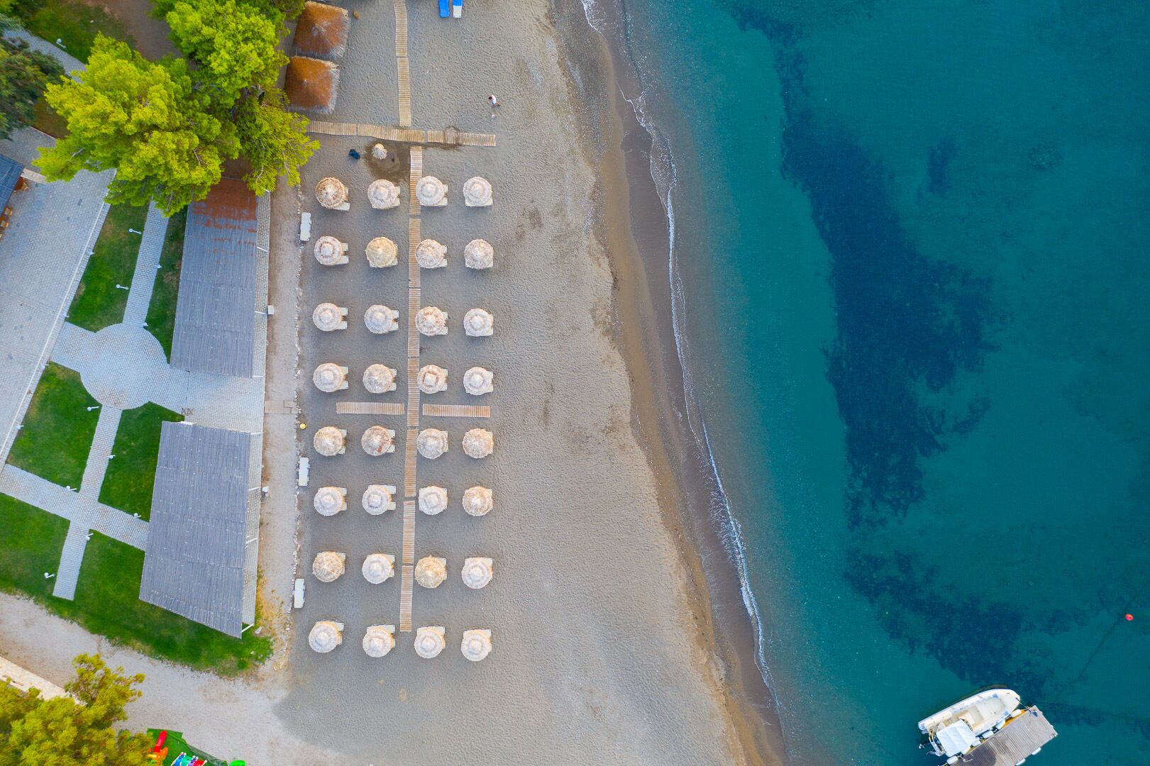 Vista aèria d'una platja amb files de gandules i un vaixell amarrat a prop de la riba.