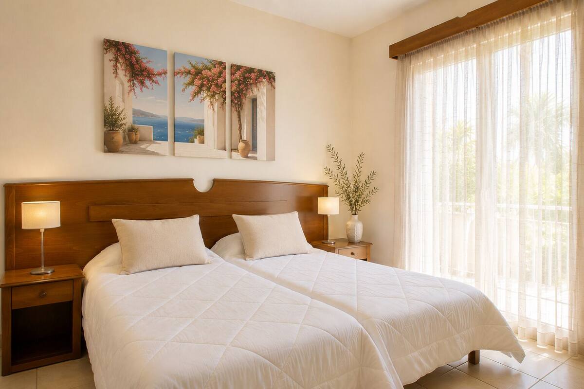 Una cama doble con dos mesitas de noche, un cabecero de madera y un ventanal con cortinas translúcidas.
