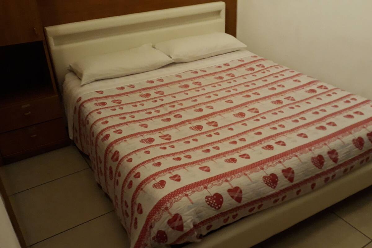 A bed with a white headboard and a patterned bedspread featuring heart designs.