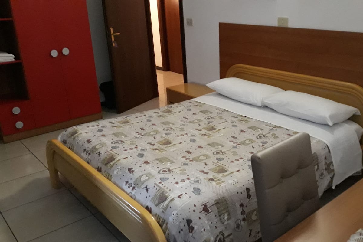 A bed with a patterned bedspread, a wooden headboard, and a bedside table with a lamp.