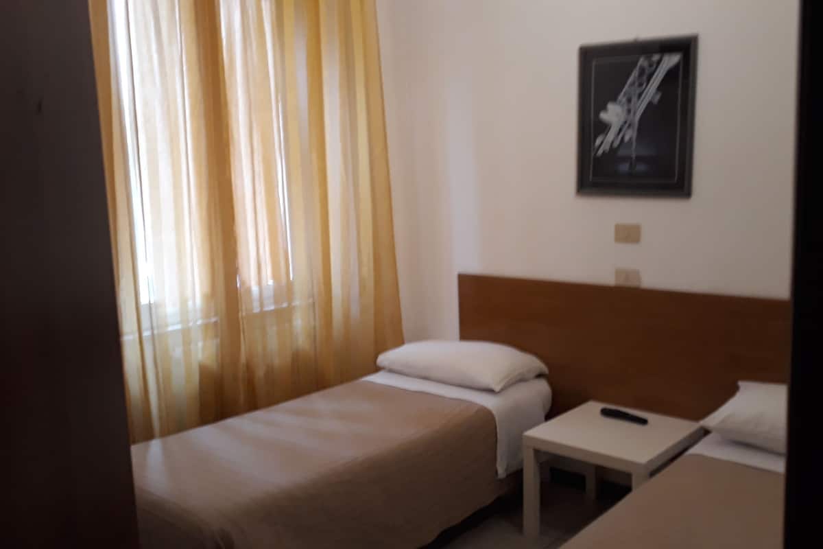 A hotel room with two single beds, a small bedside table, and a nightstand.