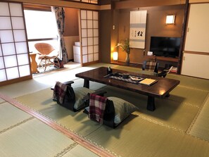A traditional Japanese-style room with tatami flooring, a low table with cushions, a television, and a sliding door. - Kappo Ryokan Satsuki (Aomori)