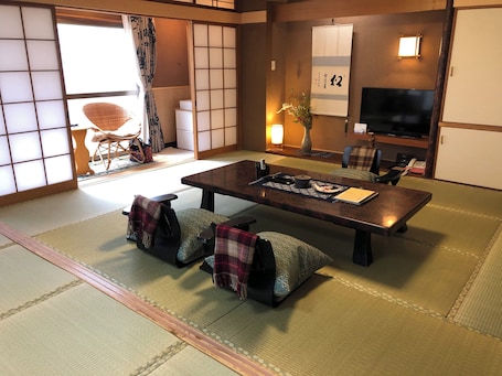 A traditional Japanese-style room with tatami flooring, a low table with cushions, a television, and a sliding door.
