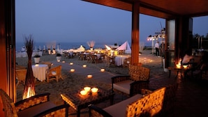 An outdoor dining area with tables and chairs, a view of the beach, and a fire pit. - Hotel President (Silvi)