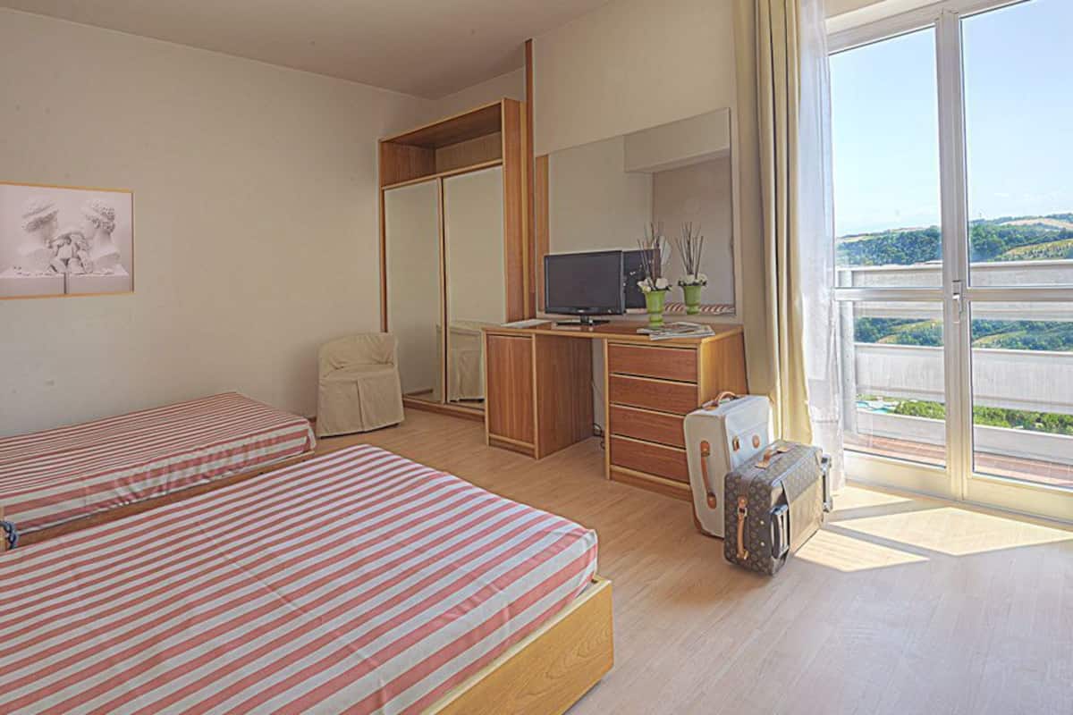 A hotel room with two beds, a desk, a TV, and a suitcase.