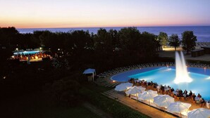 Zona de piscina con fuente, rodeada de sillas de descanso y sombrillas, con vista a la playa.