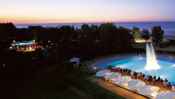 A pool area with a fountain, surrounded by lounge chairs and umbrellas, overlooking a beach. - Hotel President (Silvi)