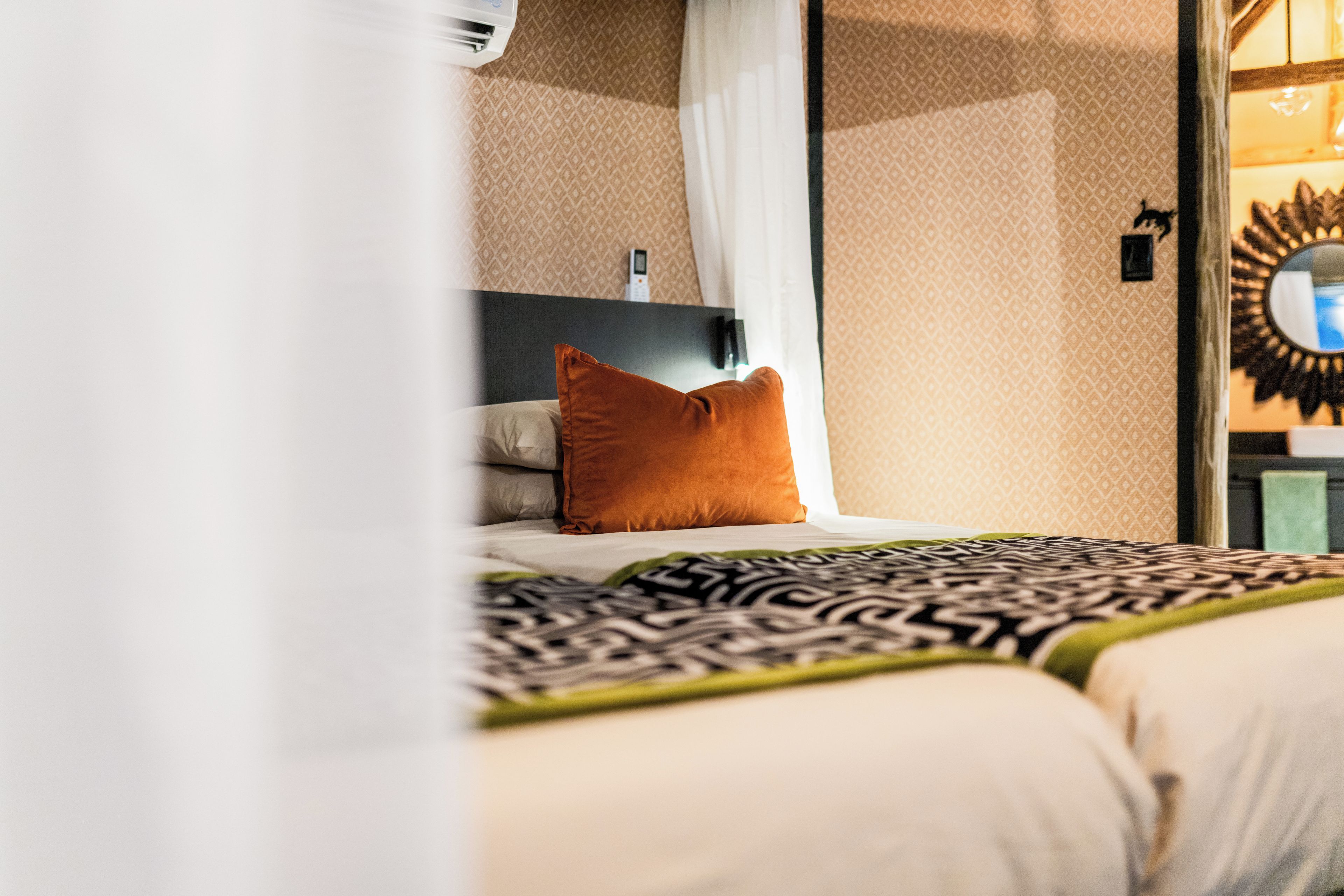 A hotel room with a bed, a nightstand, a mirror, and a wall-mounted telephone.