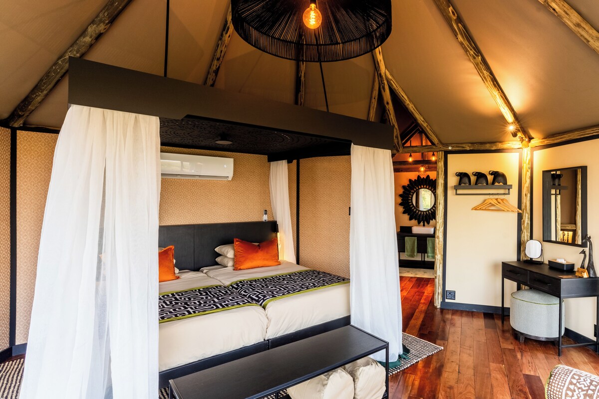 Quarto com cama de dossel, mesa de cabeceira e escrivaninha com cadeira.
