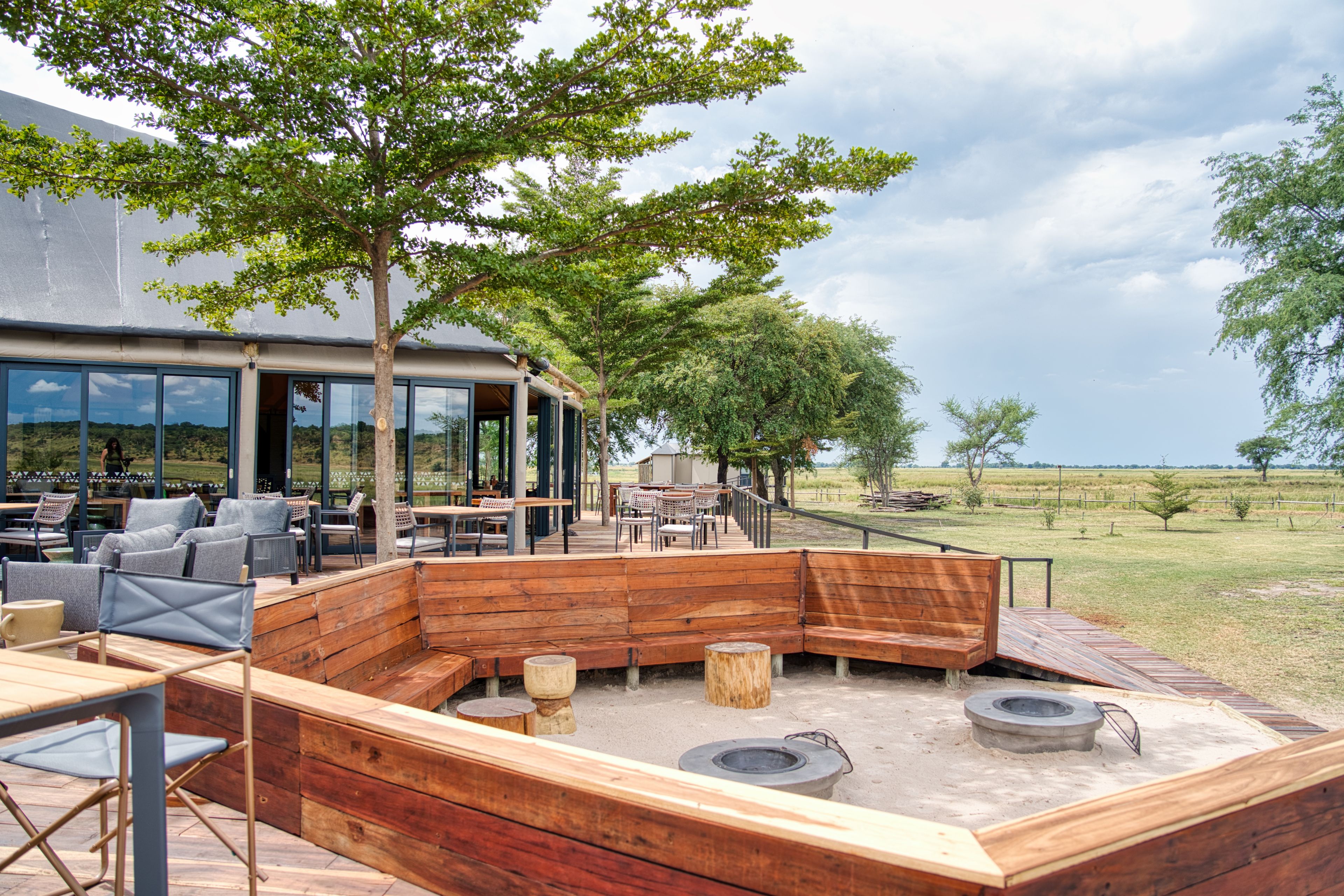 An outdoor seating area with wooden benches and tables, a fire pit, and a view of the surrounding landscape.