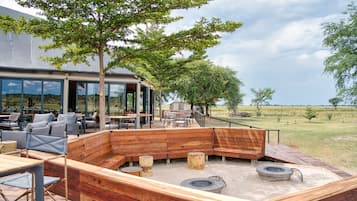 An outdoor seating area with wooden benches and tables, a fire pit, and a view of the surrounding landscape.