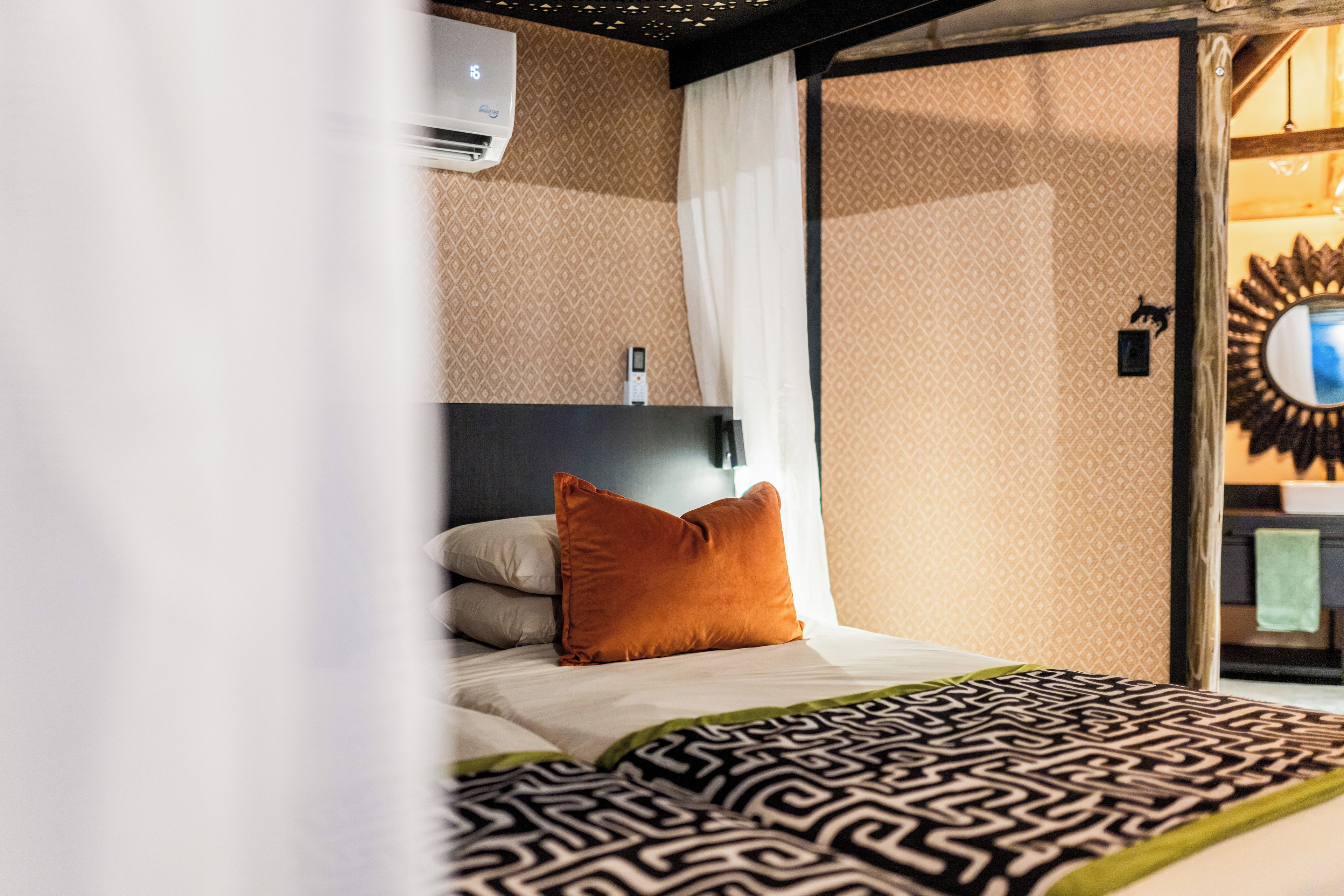 Habitación de hotel con una cama, aire acondicionado de pared, espejo y colcha estampada.
