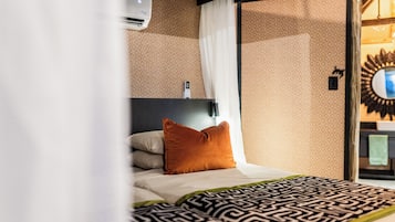 Habitación de hotel con una cama, aire acondicionado de pared, espejo y colcha estampada.