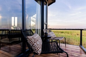 Une terrasse avec des chaises et une table en osier, donnant sur un champ verdoyant.