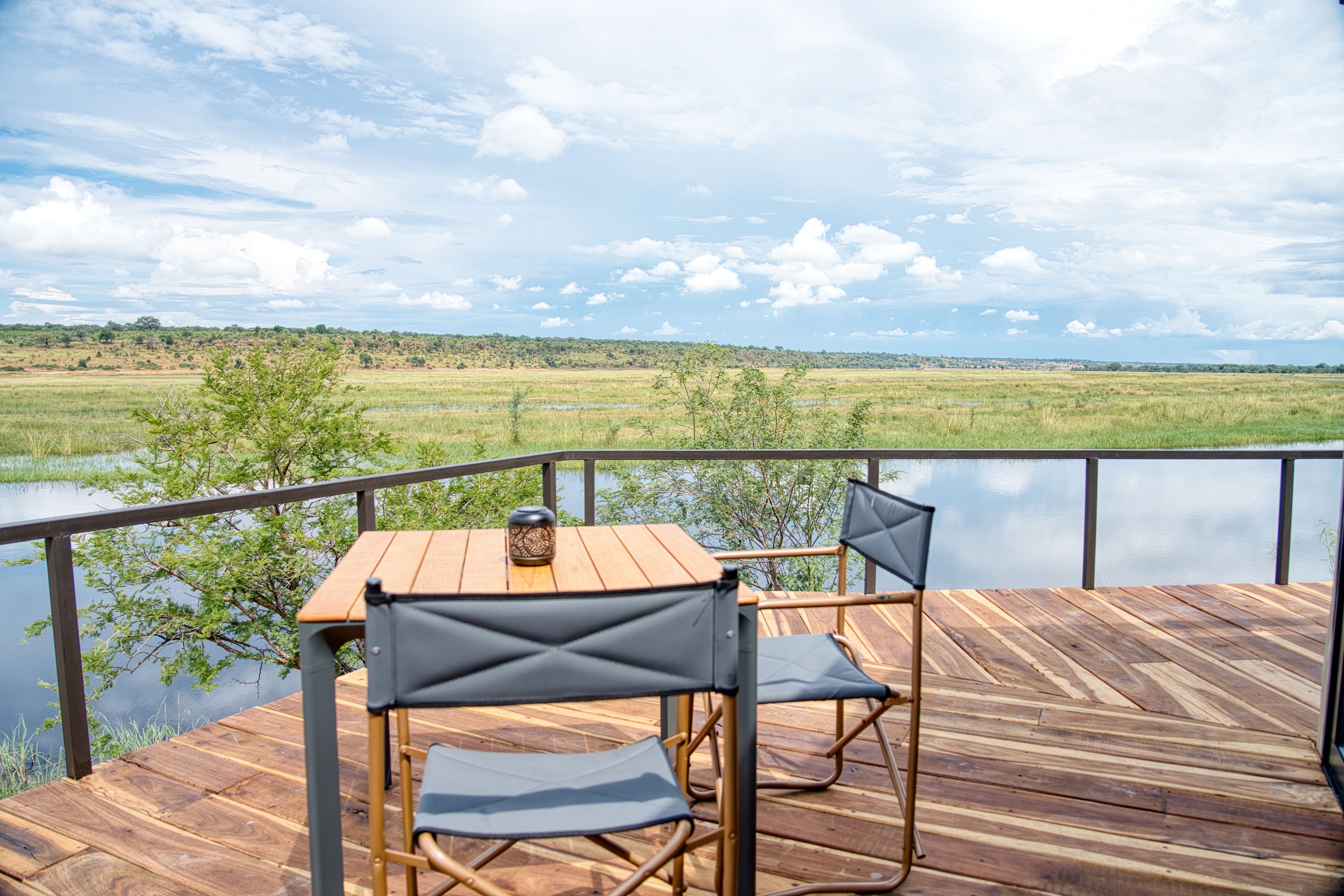A wooden deck with a table and chairs overlooking a lake and distant landscape.
