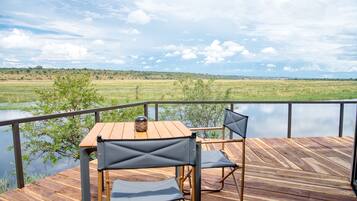 A wooden deck with a table and chairs overlooking a lake and distant landscape.