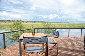A wooden deck with a table and chairs overlooking a lake and distant landscape.